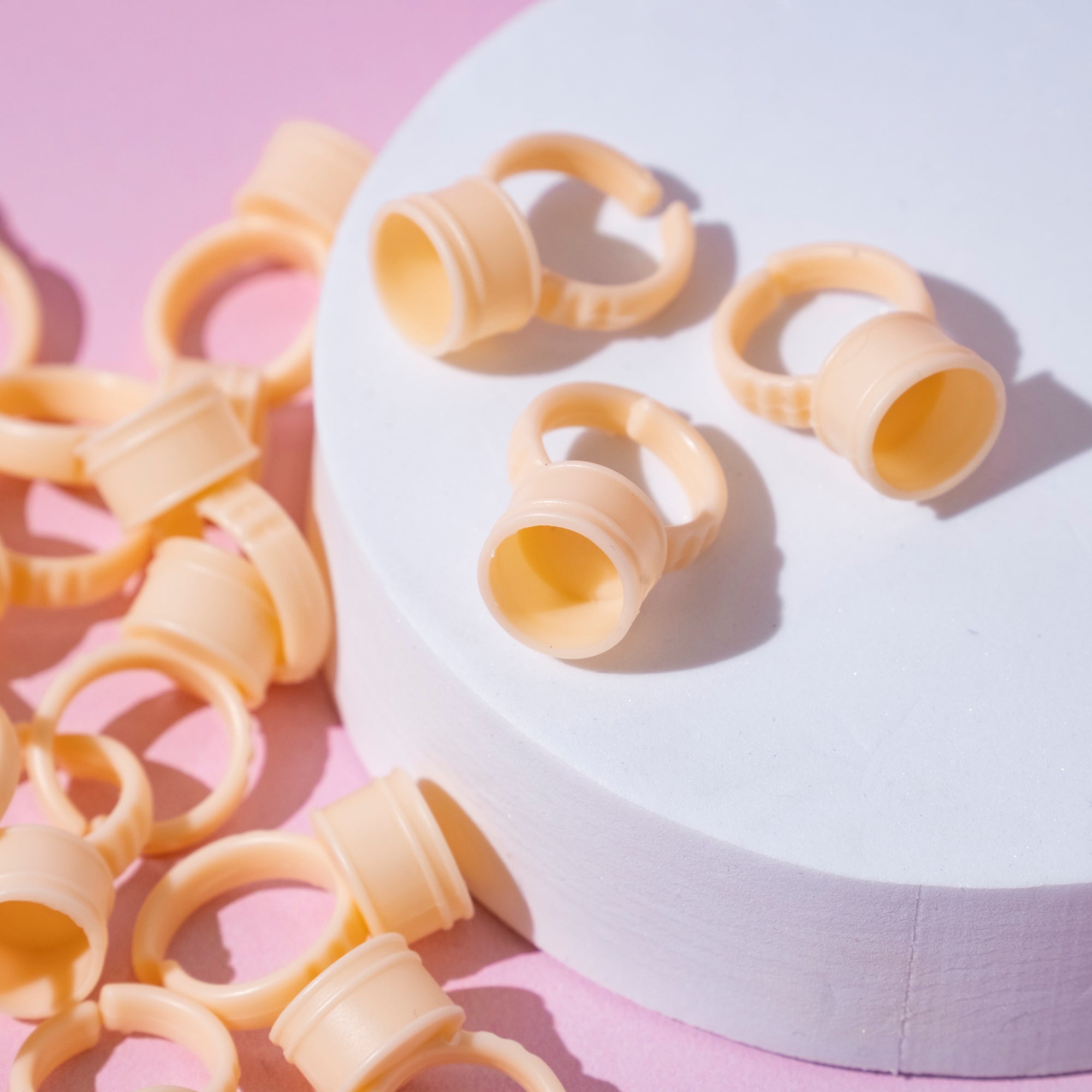 Silicon Glue Rings scattered on a pink surface with some displayed on a white circular platform.