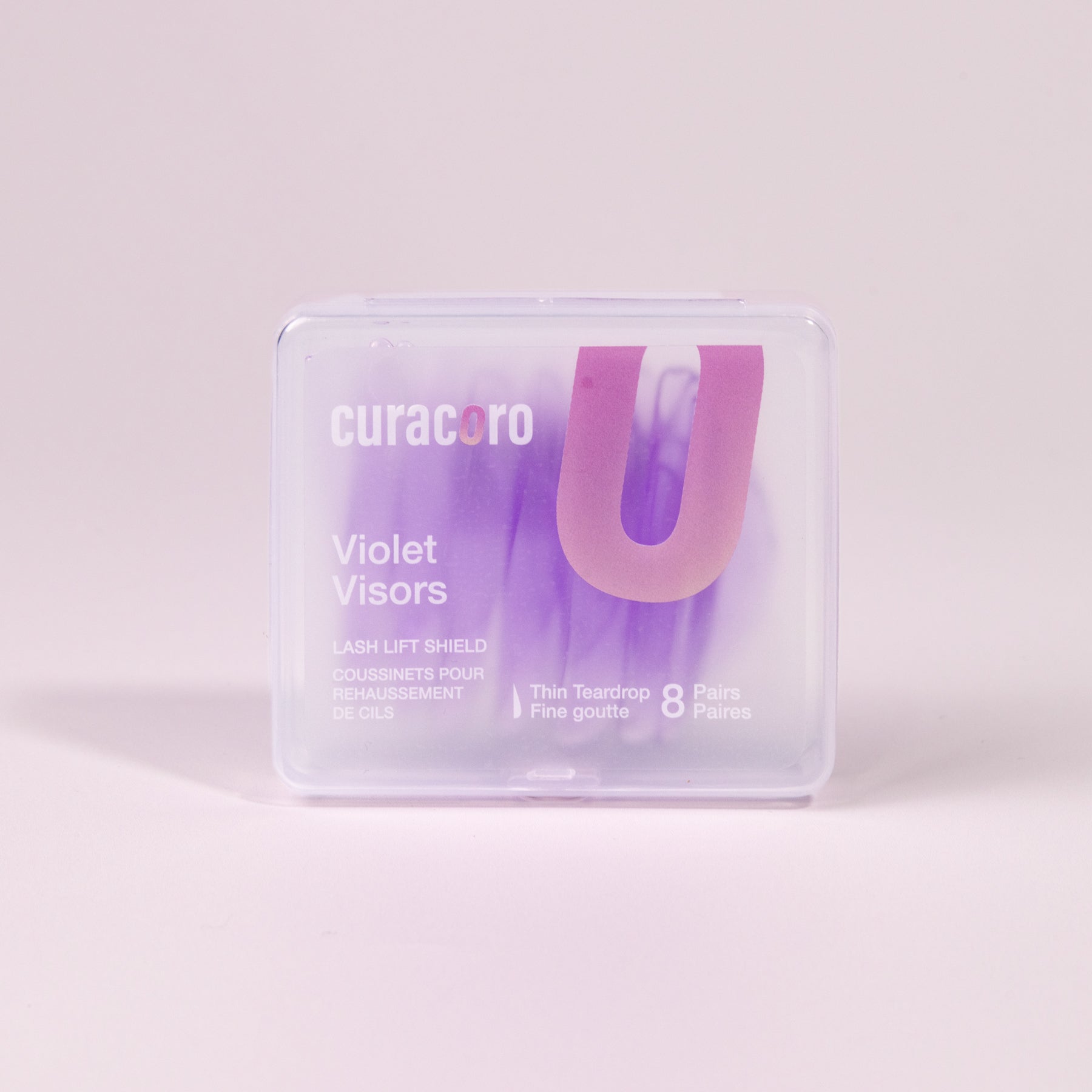 Curacoro Violet Visors lash lift shields in a transparent case featuring 8 pairs of thin teardrop-shaped shields. on a soft pink background.