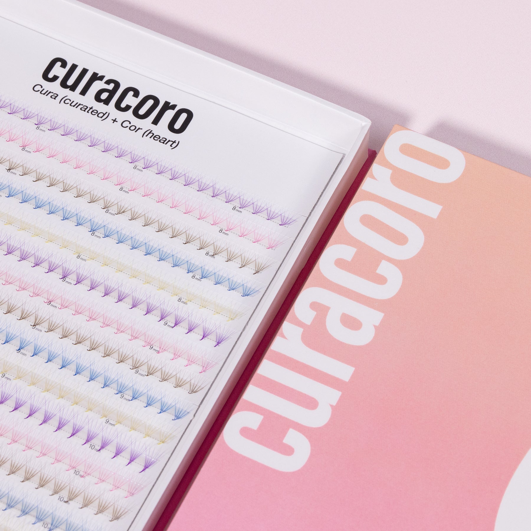 Curacoro Rainbow Promade Fans XL tray showcasing multi-colored lash extensions in an open box with a gradient pink background.