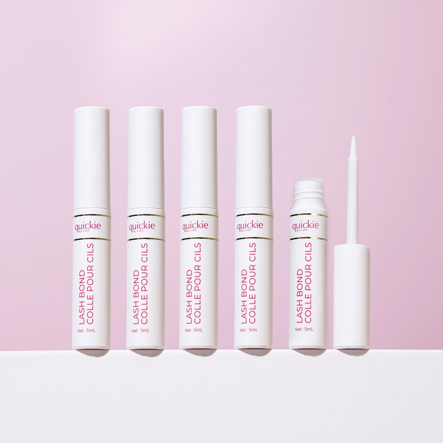 Five lash bond tubes with white packaging, one open with the applicator visible, arranged on a white surface against a light purple background.