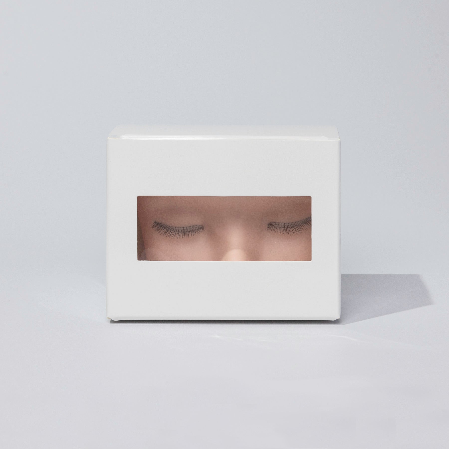 Mannequin head with multi-layered eyelash extensions, displayed inside a sleek white packaging box with a transparent window.