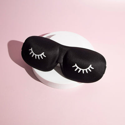 Black coloured 3D Contoured Sleep Masks in front of a pink background..