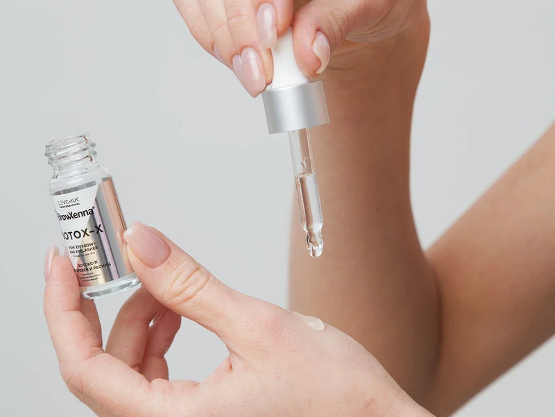 Bottle of lash and brow botox held in hand with dropper and a drop of product