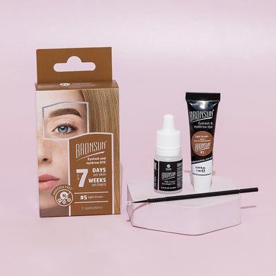 Eyelash and eyebrow light brown dye tube, milk cream developer, and microbrush displayed with packaging aside