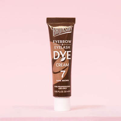 Dark brown eyebrow and eyelash dye cream tube displayed on pink background