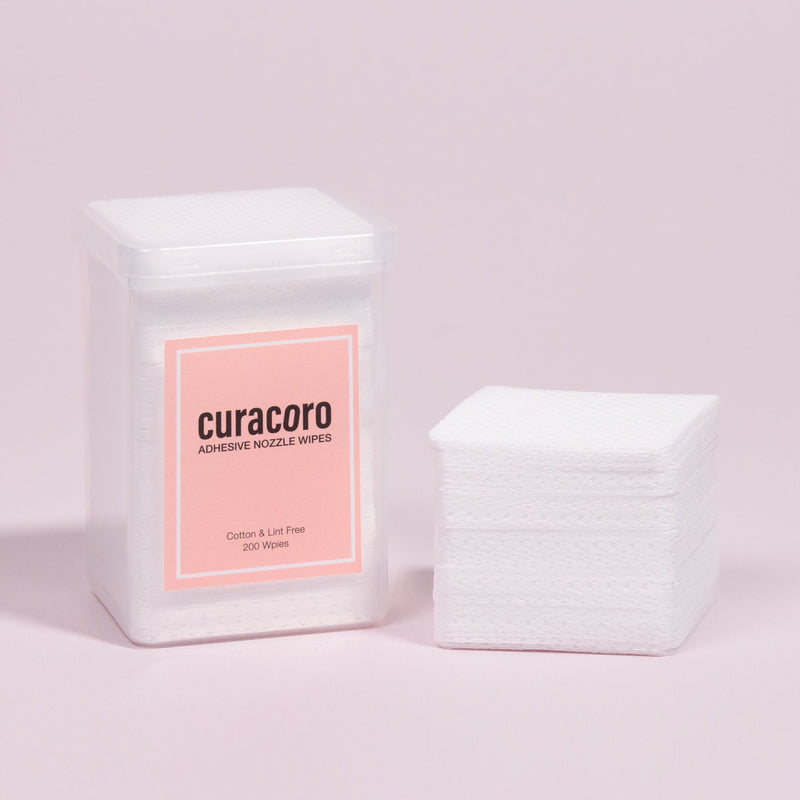 Container and stack of Curacoro adhesive nozzle wipes, displayed against a soft pink background.