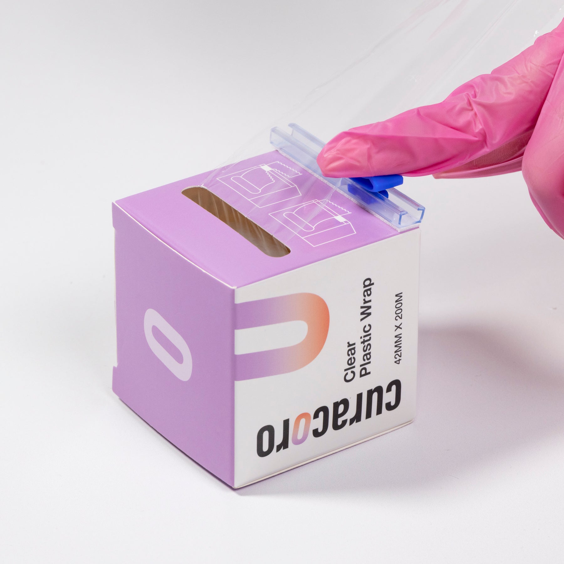 Gloved hand using the cutter on Curacoro clear plastic wrap packaging, 42mm x 200m, for brow lamination.