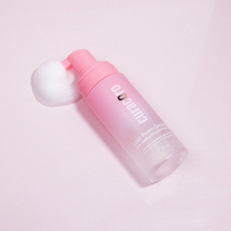 Curacoro Lash Foam Bath 60ml - Rose Scent, lying on a light pink surface, surrounded by foam.