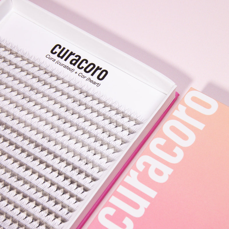 Close-up of Curacoro XL Promade Fans with Camellia lashes in an open tray on a pink background.