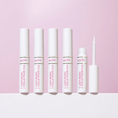 Five lash bond tubes with white packaging, one open with the applicator visible, arranged on a white surface against a light purple background.