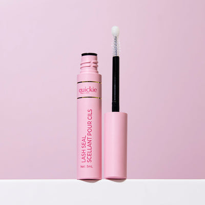 An open tube of Quickie by LLBA Lash Seal, revealing the applicator wand with a white tip, set against a light pink background.