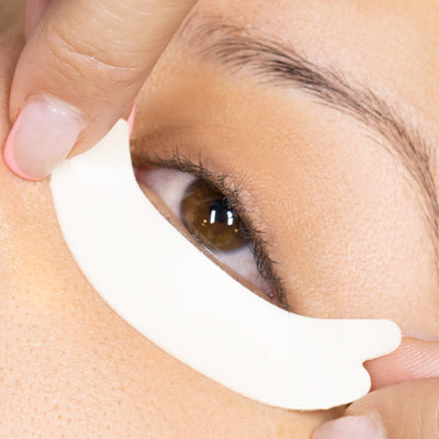 A close-up of a model's closed eye with a hypoallergenic foam under-eye pad applied to the lower eyelid, emphasizing comfort and fit.