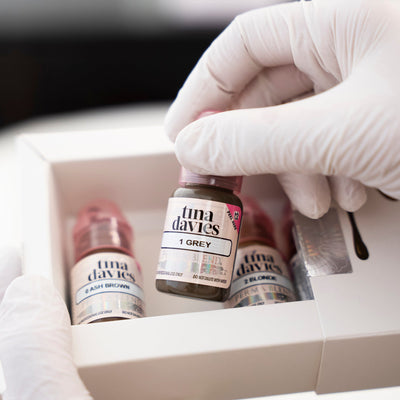 Brow pigment bottle held in hand with additional pigments in a box in the background