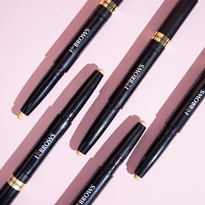 Multiple I ❤️ Brows Highlighter & Concealers in front of a pink background.