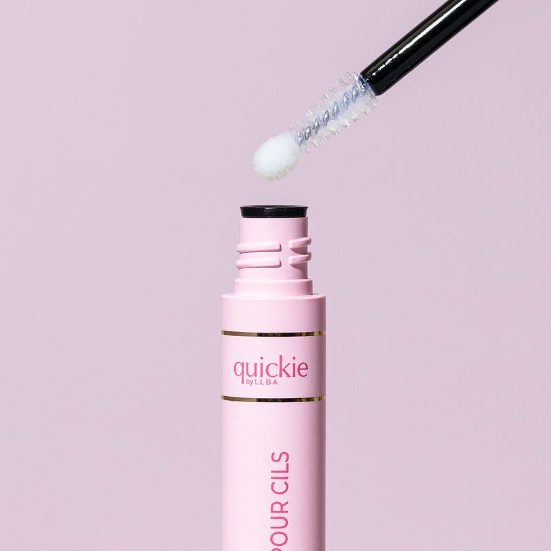 Close-up of Quickie by LLBA Lash Seal with its applicator wand partially lifted, showcasing a textured white applicator tip against a light pink background.