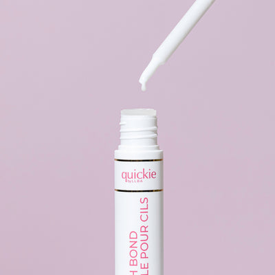 An open tube of lash bond with a white applicator dripping a small amount, set against a light purple background.