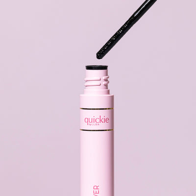 Pink tube of Quickie by LLBA Remover with wand applicator partially lifted, showing close-up details, against a soft pink background.