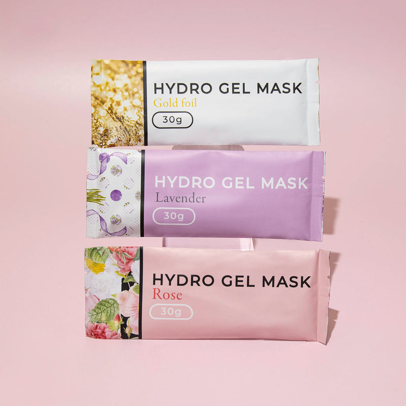 Three varieties of Hydro Gel Mask packages, stacked vertically: Gold Foil, Lavender, and Rose, each weighing 30g, displayed against a light pink background.