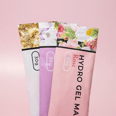 Three varieties of Hydro Gel Mask packages, stacked vertically: Gold Foil, Lavender, and Rose, each weighing 30g, displayed against a light pink background.