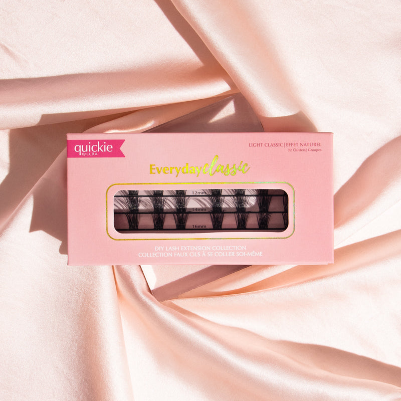 Pink lash extension kit box with transparent window showing three rows of lash clusters in different lengths, placed on soft, peach-colored fabric.