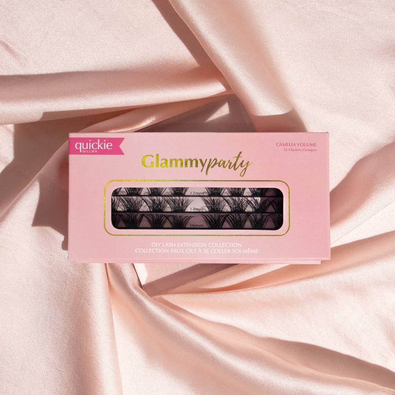 Pink lash extension kit box with transparent window showing three rows of lash clusters in different lengths, placed on soft, peach-colored fabric.