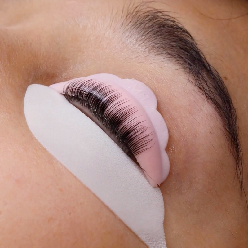 Close-up of eyelashes curled on a pink silicone pad, with a white under-eye patch in place.