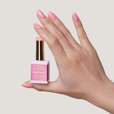 LLBA Peach Parfait Gel Polish bottle held in a hand, showcasing a soft pink shade on nails with a glittery finish against a light background."