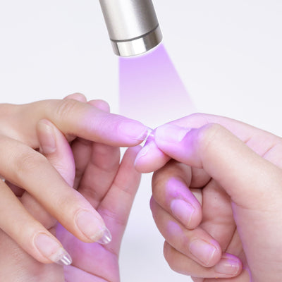 Close-up of hands using a Cordless UV/LED Light for Gel Nail Polish to cure nail extensions, with the UV light shining on the nails during the process.