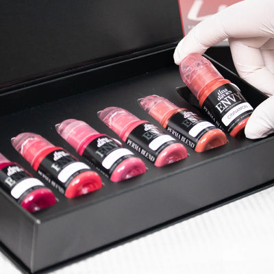 Tina Davies Envy Lip Pigment Collection open box with six pigment bottles, one being picked up by a gloved hand.