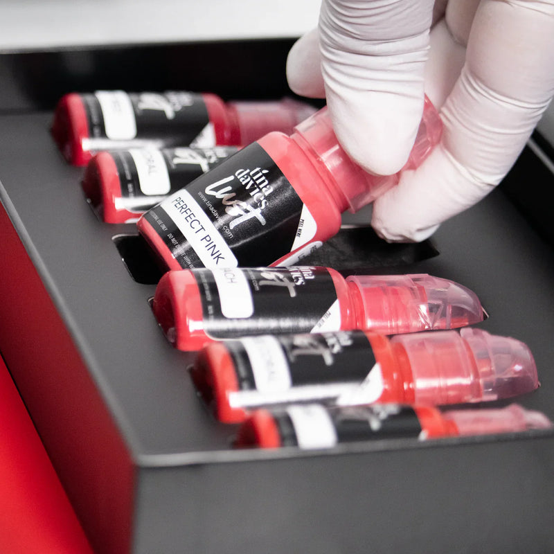 Gloved hand holding a Tina Davies Lust lip pigment bottle labeled "Perfect Pink" from a black box set.