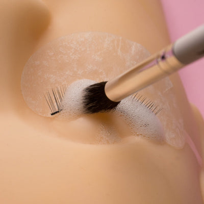 Extended wooden cleansing brush being used to clean mannequin lashes.