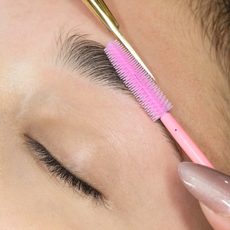 Image of using a disposable pink silicon brush to shape eyebrows.